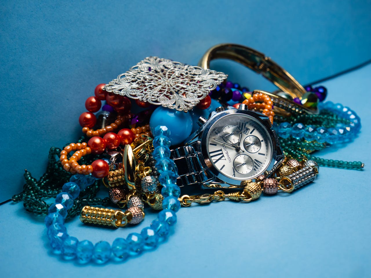 A close-up shot of various colorful jewelry pieces with a stylish wristwatch on blue background.